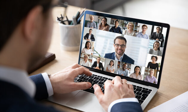 Mann am Laptop kommuniziert per Videchat mit einer Gruppe von Personen