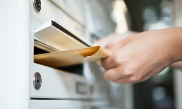 Großer Briefumschlag wird per Hand in den Briefkasten eingeworfen