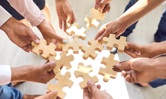 Mehrere Hände halten jeweils ein Puzzleteil in den Händen