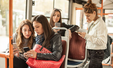 Eine Gruppe junger Frauen konsumiert Inhalte auf dem Smartphone während der Fahrt im ÖPNV 
