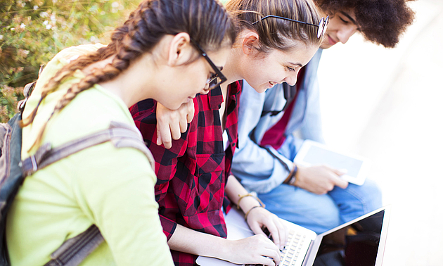 Bild von drei jungen Menschen, die auf ein Laptop blicken