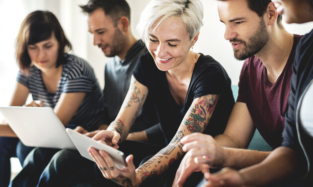 Gruppe junger Leute arbeitet gemeinsam an Laptop und Tablet