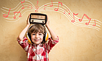 Kleiner junge mit Kopfhörern hält ein Retro-Radio über den Kopf aus dem Noten kommen