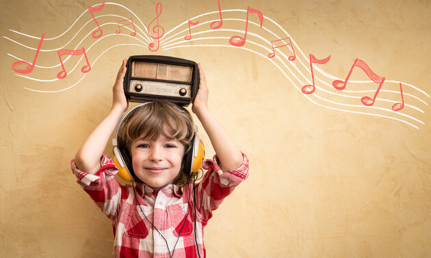 Kleiner junge mit Kopfhörern hält ein Retro-Radio über den Kopf aus dem Noten kommen