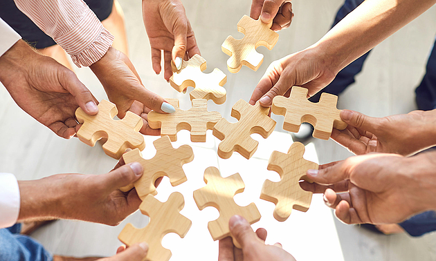 Viele Hände fügen Puzzleteile zusammen